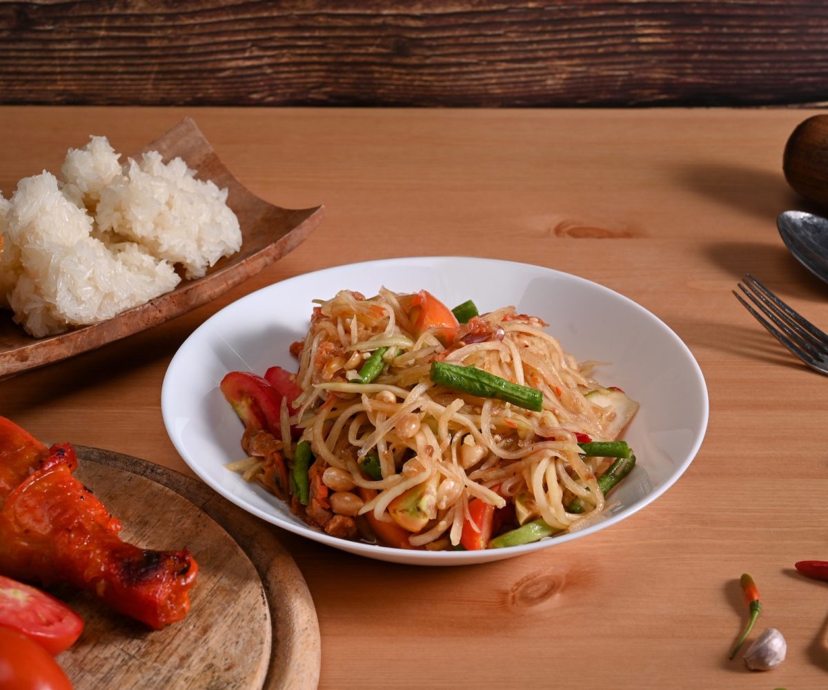 Traditional Thai food papaya salad in white plate on wooden background. Thai food concept.